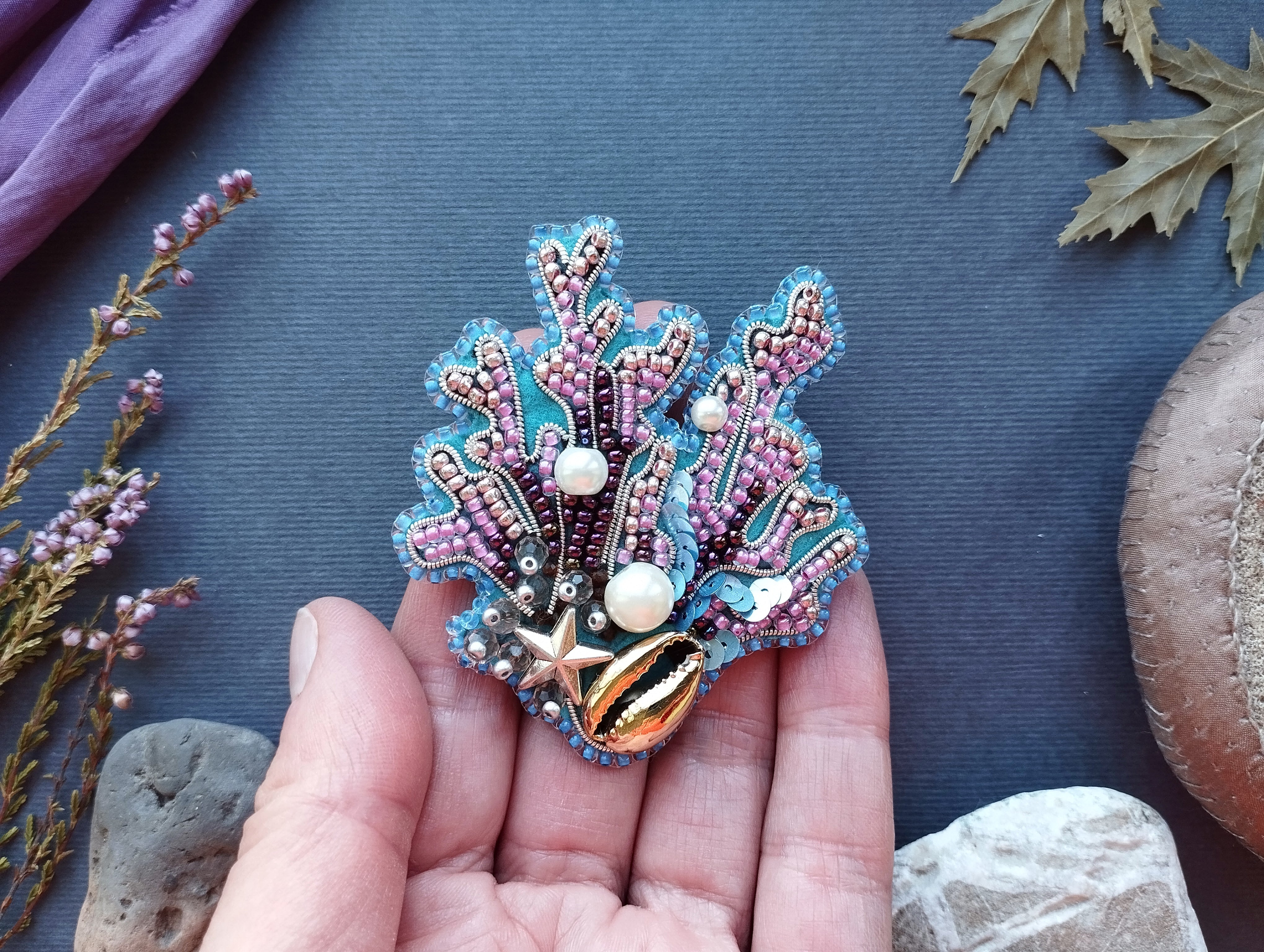 A hand holding a colorful, intricately beaded brooch or pin against a dark background.
