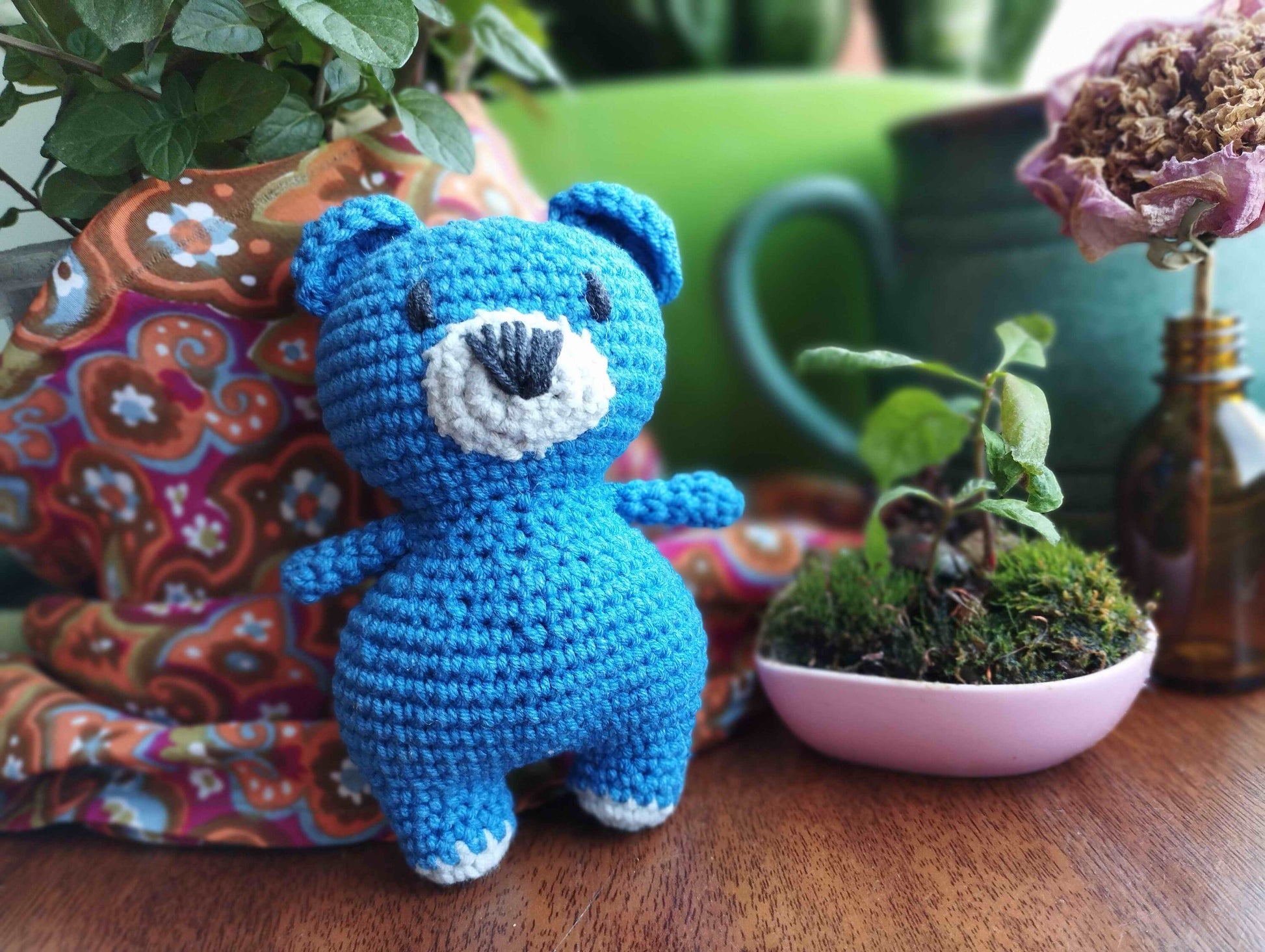 a crocheted blue teddy bear next to a potted plant