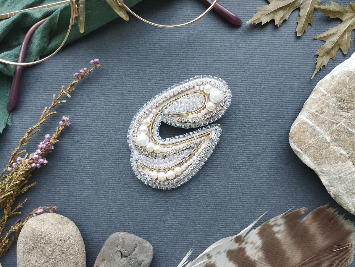 a close-up of a decorative letter 'E' made of jewels and pearls, surrounded by various natural elements such as feathers, rocks, and leaves.