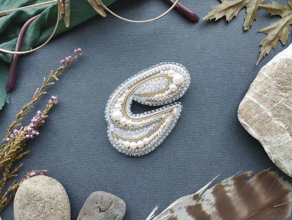 a close-up of a decorative letter 'E' made of jewels and pearls, surrounded by various natural elements such as feathers, rocks, and leaves.