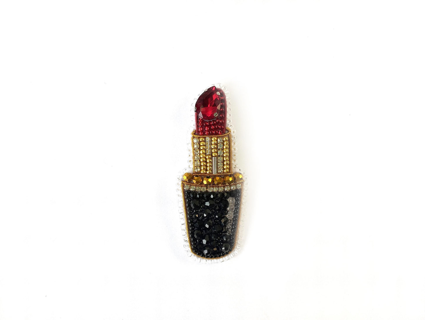 A decorative piece featuring a red lipstick with a gold and black design, including rhinestones and a gemstone.