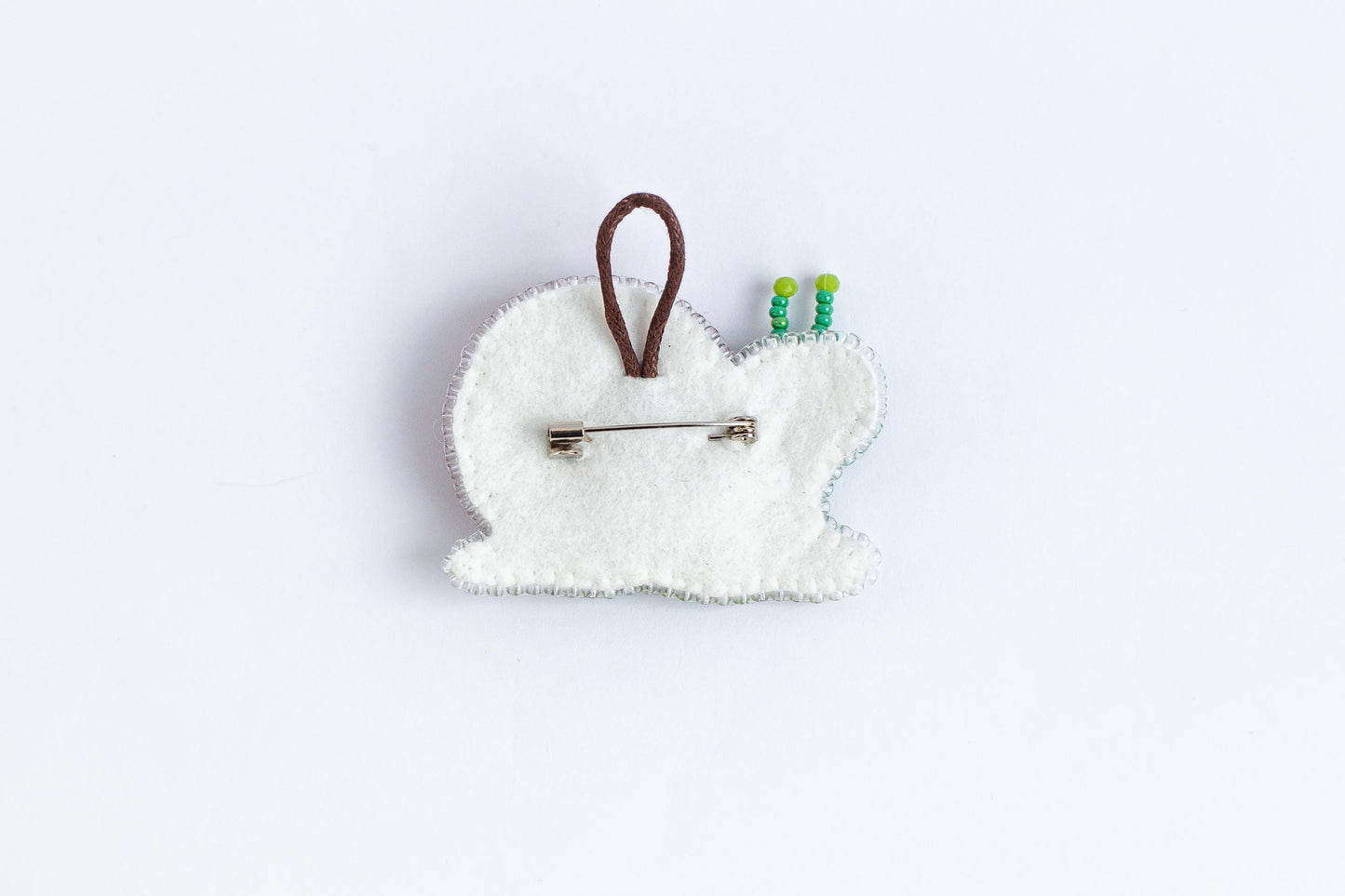 A white felt object with a brown loop and green beads attached to it, placed against a plain white background.