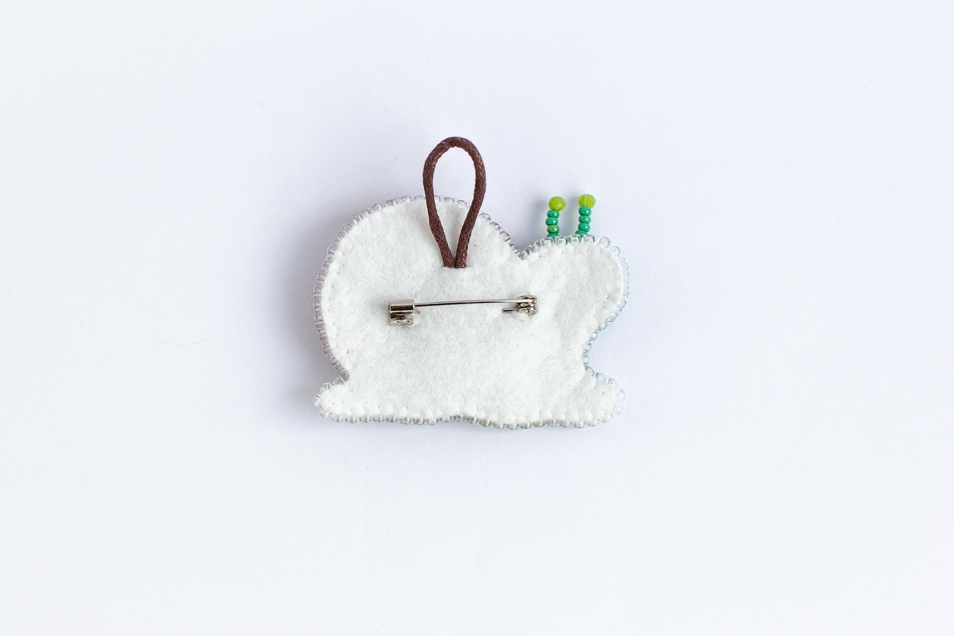 A white felt object with a brown loop and green beads attached to it, placed against a plain white background.