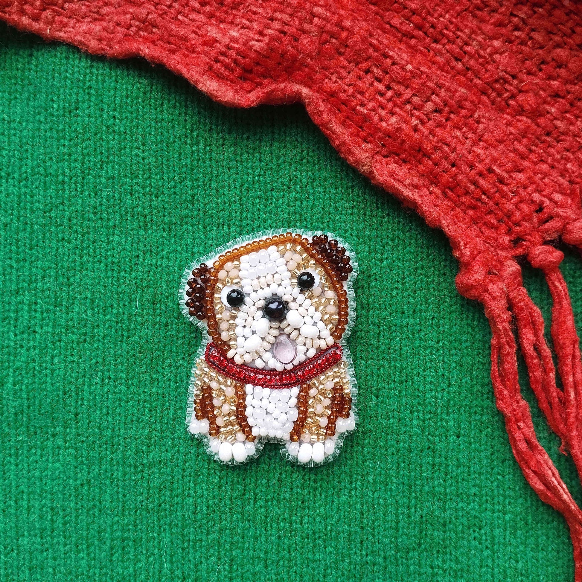 A small, intricately beaded embroidered dog is displayed on a green background, with a red fabric or material partially visible to the right.