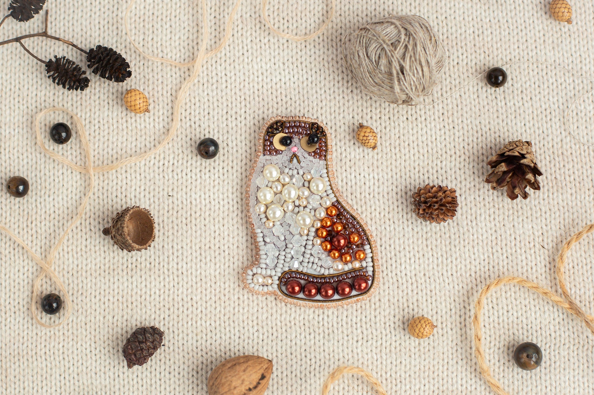 a mosaic of various objects, including a cat-shaped piece of art, pine cones, beads, and other natural elements, all arranged on a white background.