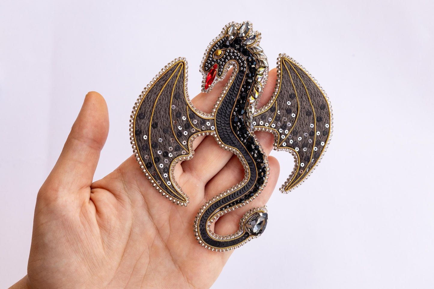 a hand is holding a dragon brooch in it&#39;s right hand