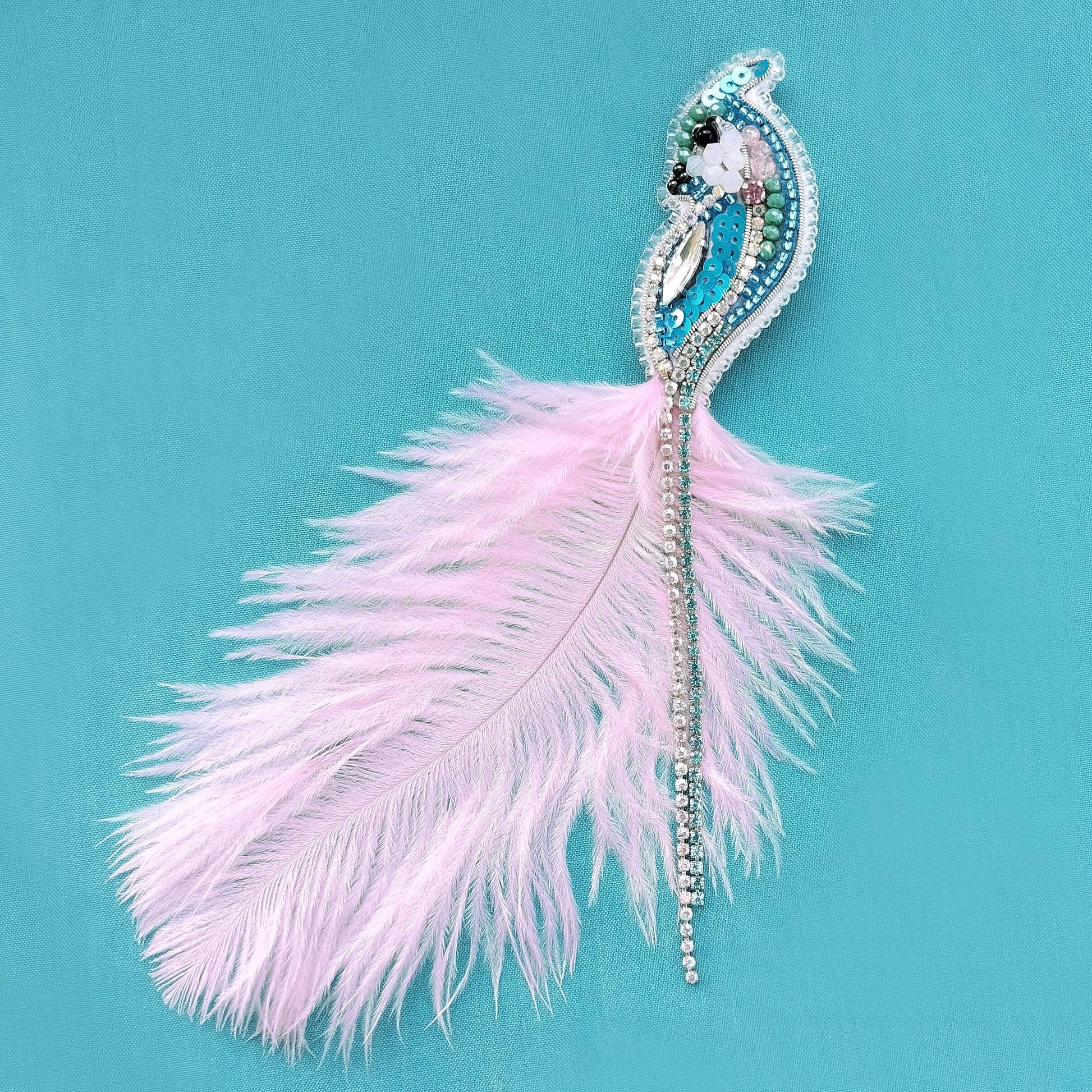 A decorative feather with a beaded and sequined design is displayed against a teal background.