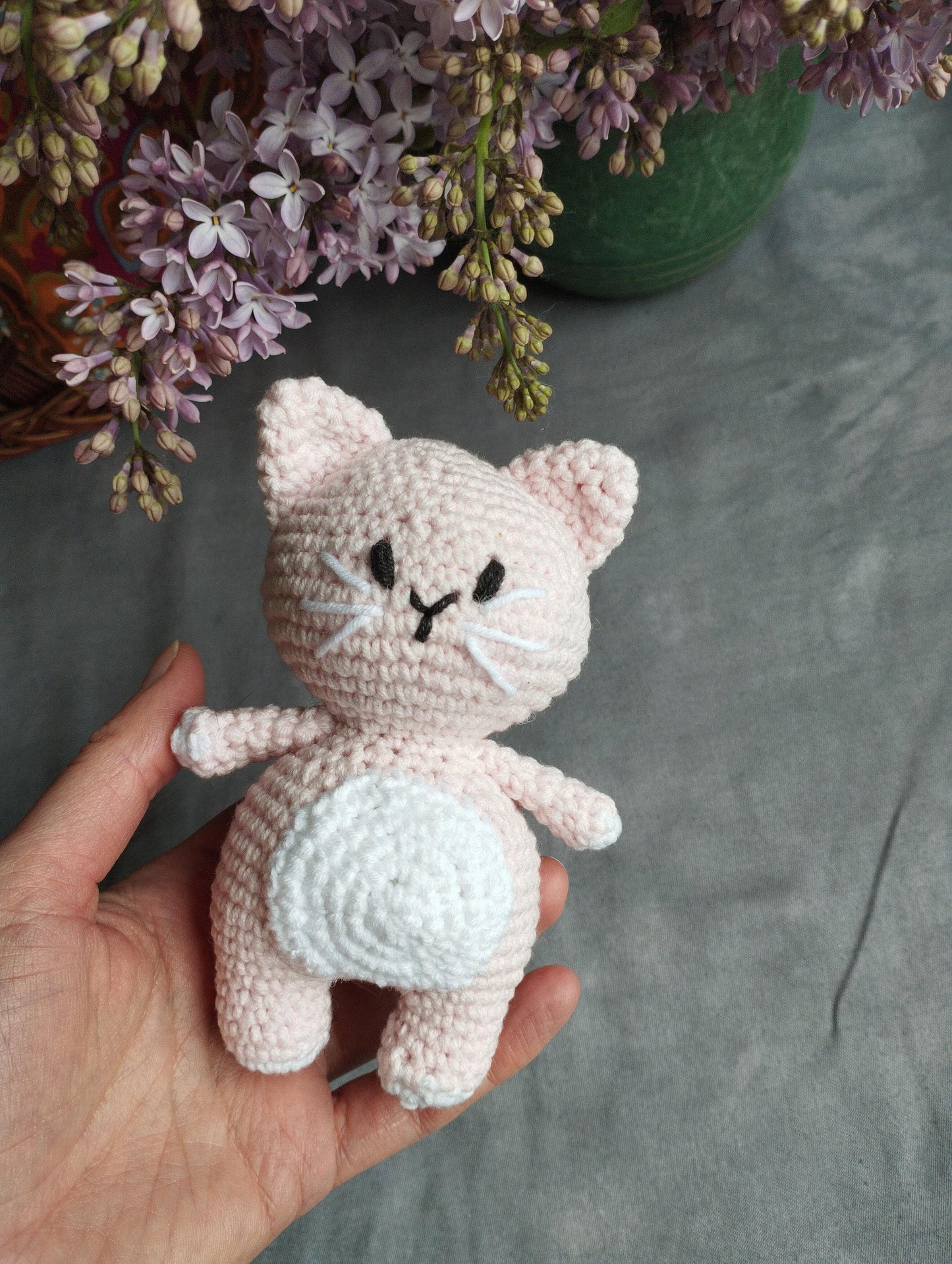 a hand holding a small crocheted cat next to a potted plant