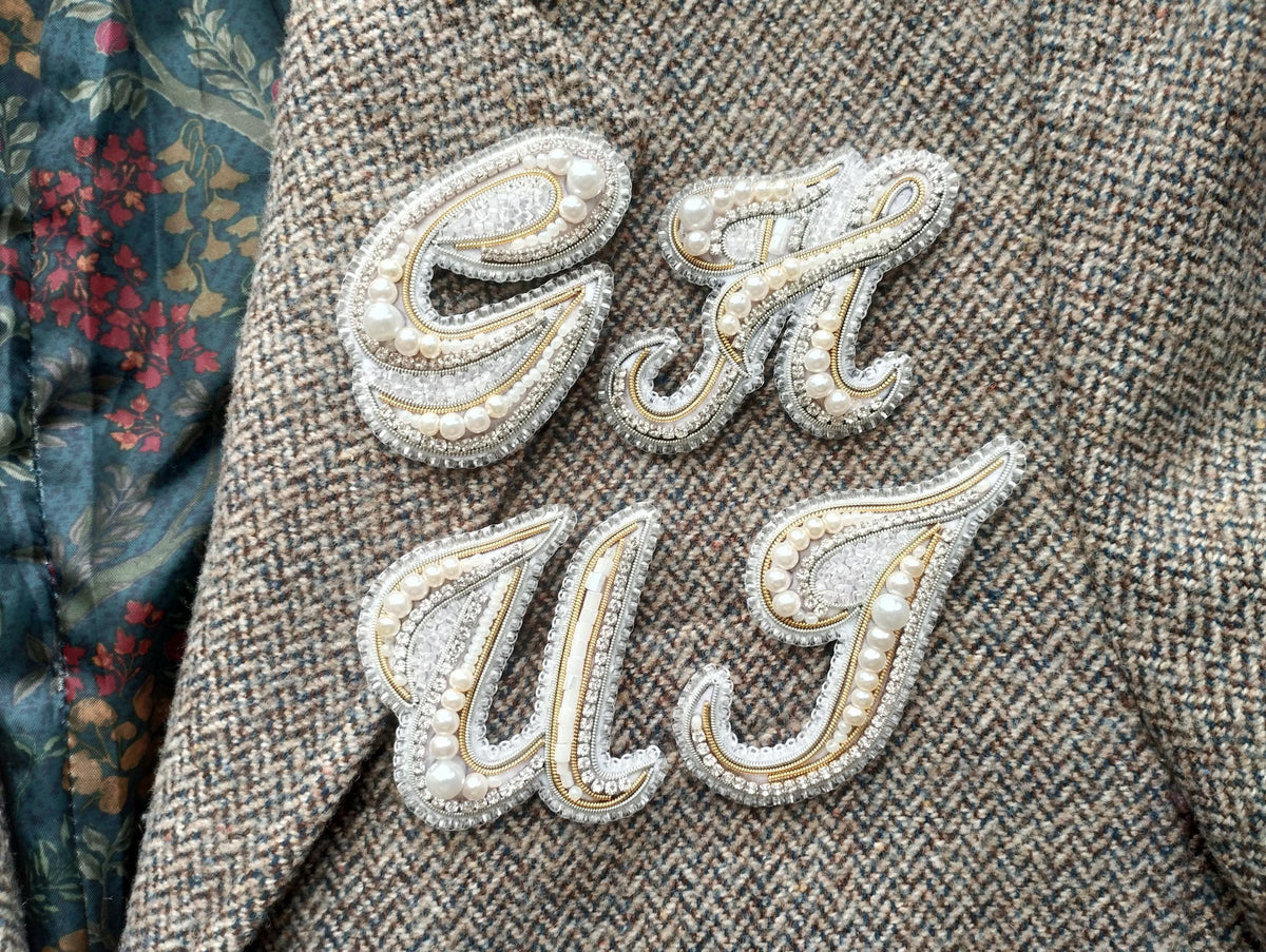 a close-up of a fabric with a decorative embroidered letter "C" and "U" attached to it, both embellished with pearls and rhinestones.