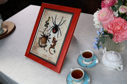 a red-framed picture of various insects, including a spider, on a table with two teacups and a vase of pink flowers.