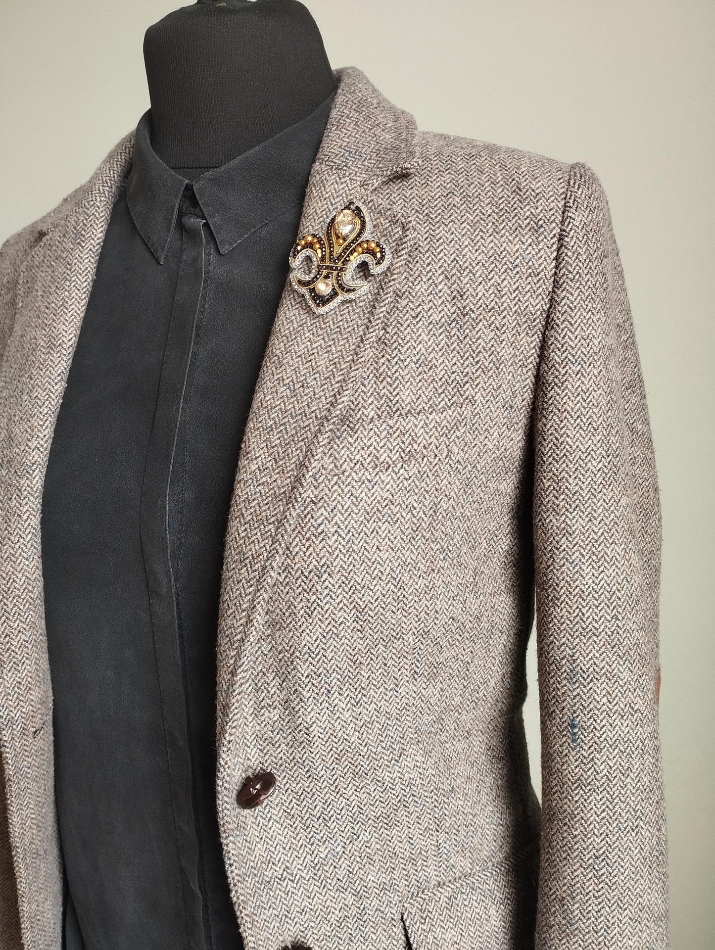 A gray tweed blazer with a black shirt underneath, and a decorative brooch on the left breast.