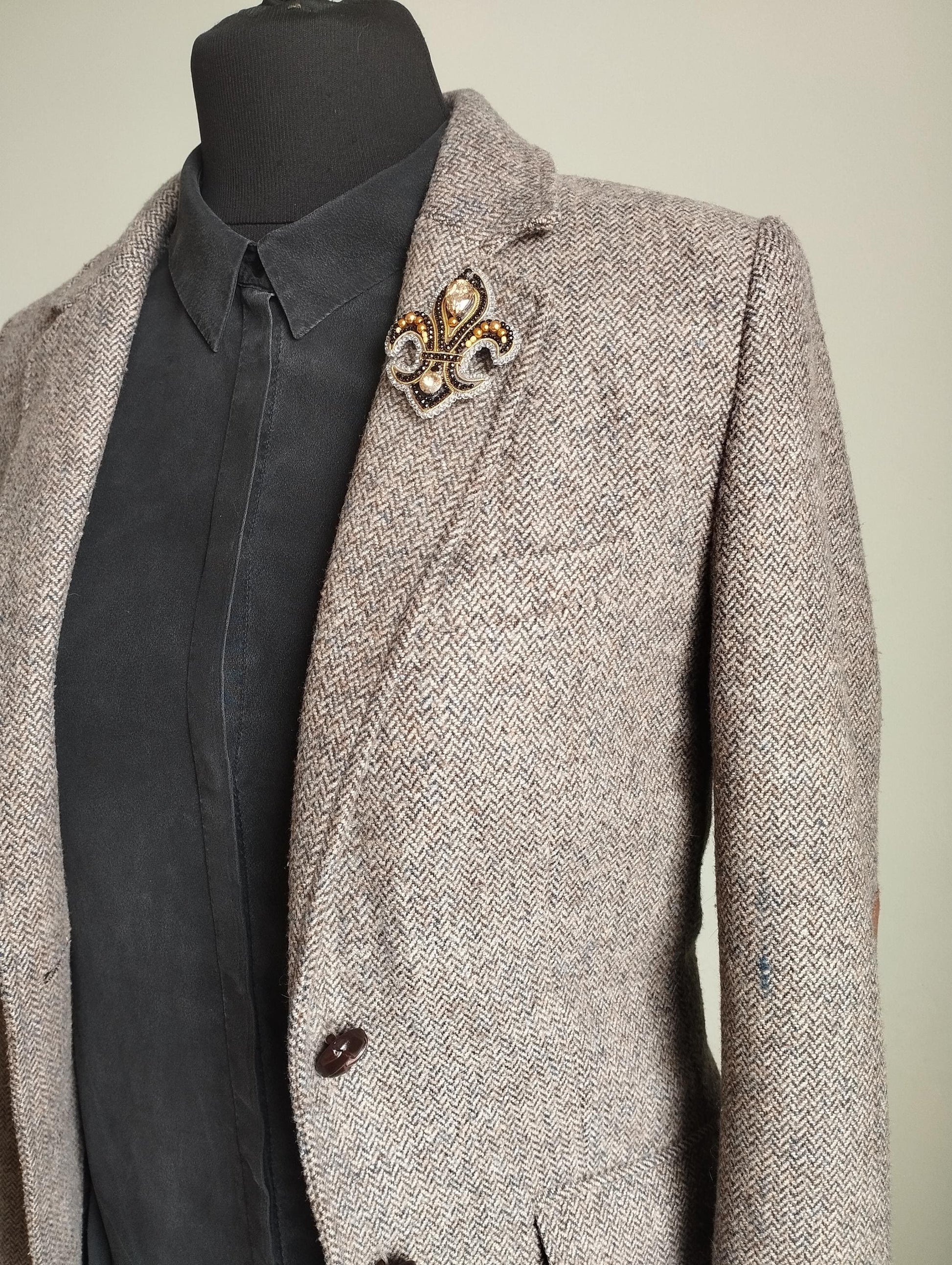 A gray tweed blazer with a black shirt underneath, and a decorative brooch on the left breast.