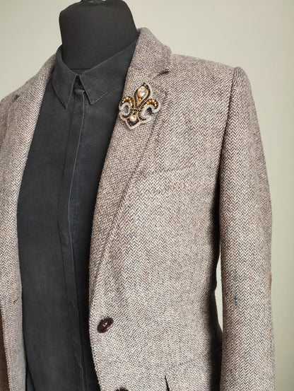 A gray tweed blazer with a black shirt underneath, and a decorative brooch on the left breast.