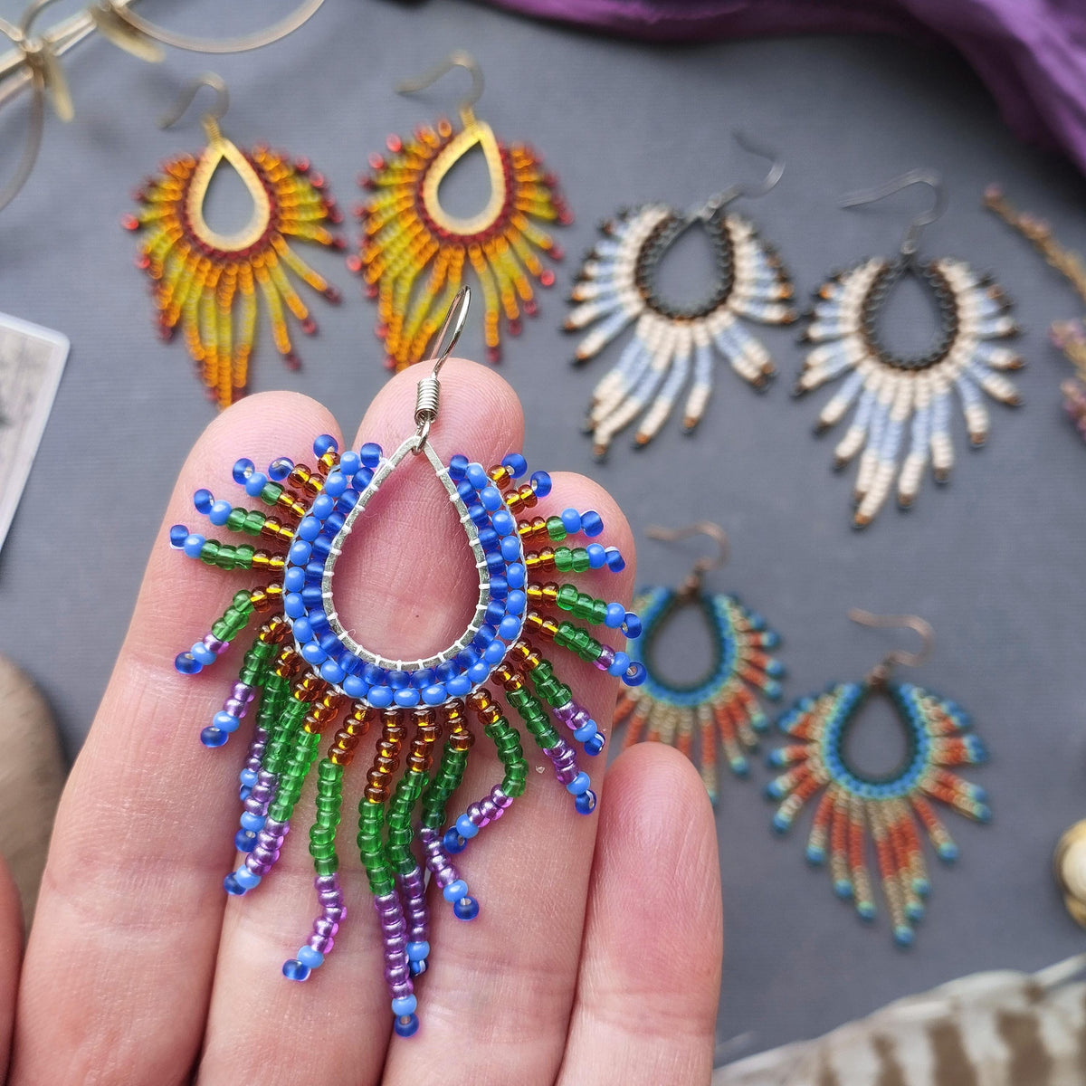 A hand holding a colorful beaded earring with a large, dangling design.