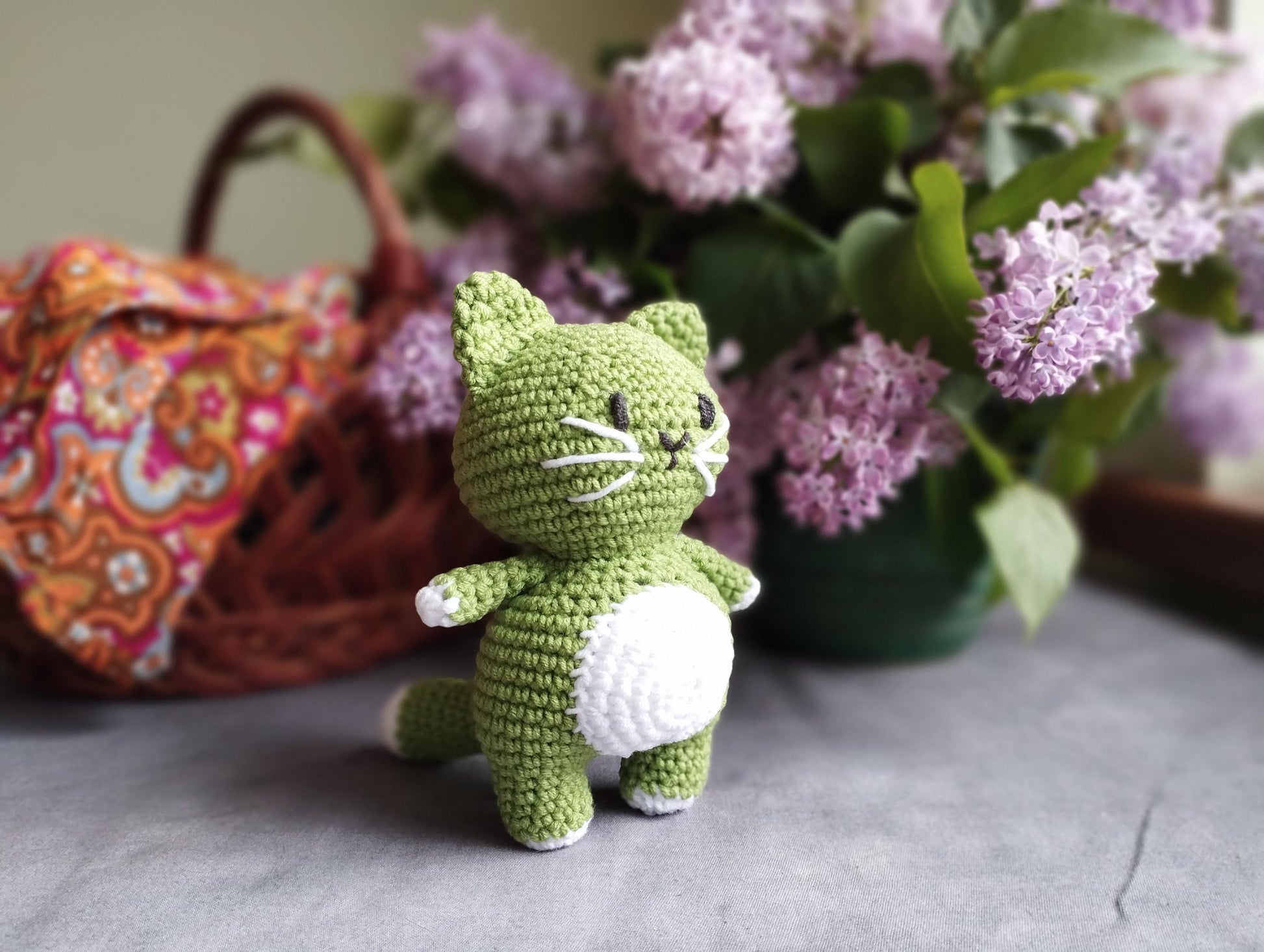 a crocheted cat sitting next to a basket of flowers