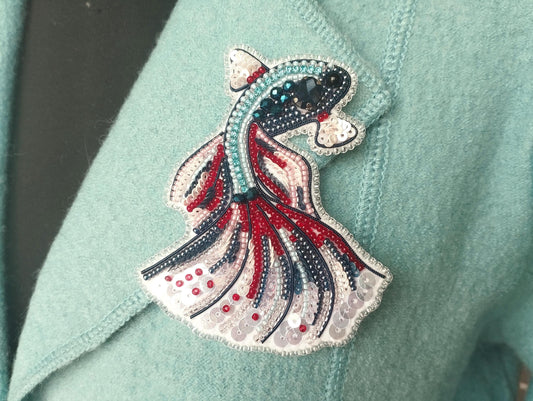 A close-up of a teal-colored fabric with a decorative beaded fish embroidered on it.