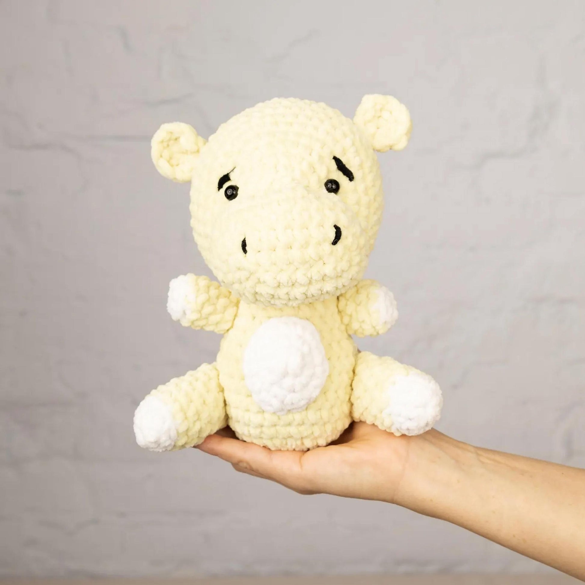 A hand holding a crocheted, yellow stuffed animal with white accents against a plain white background.