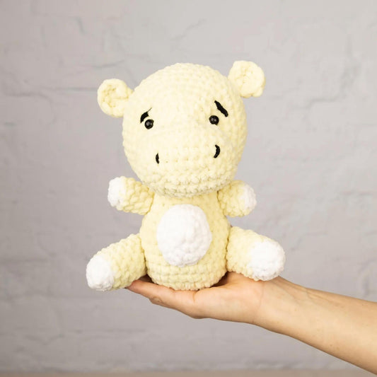 A hand holding a crocheted, yellow stuffed animal with white accents against a plain white background.