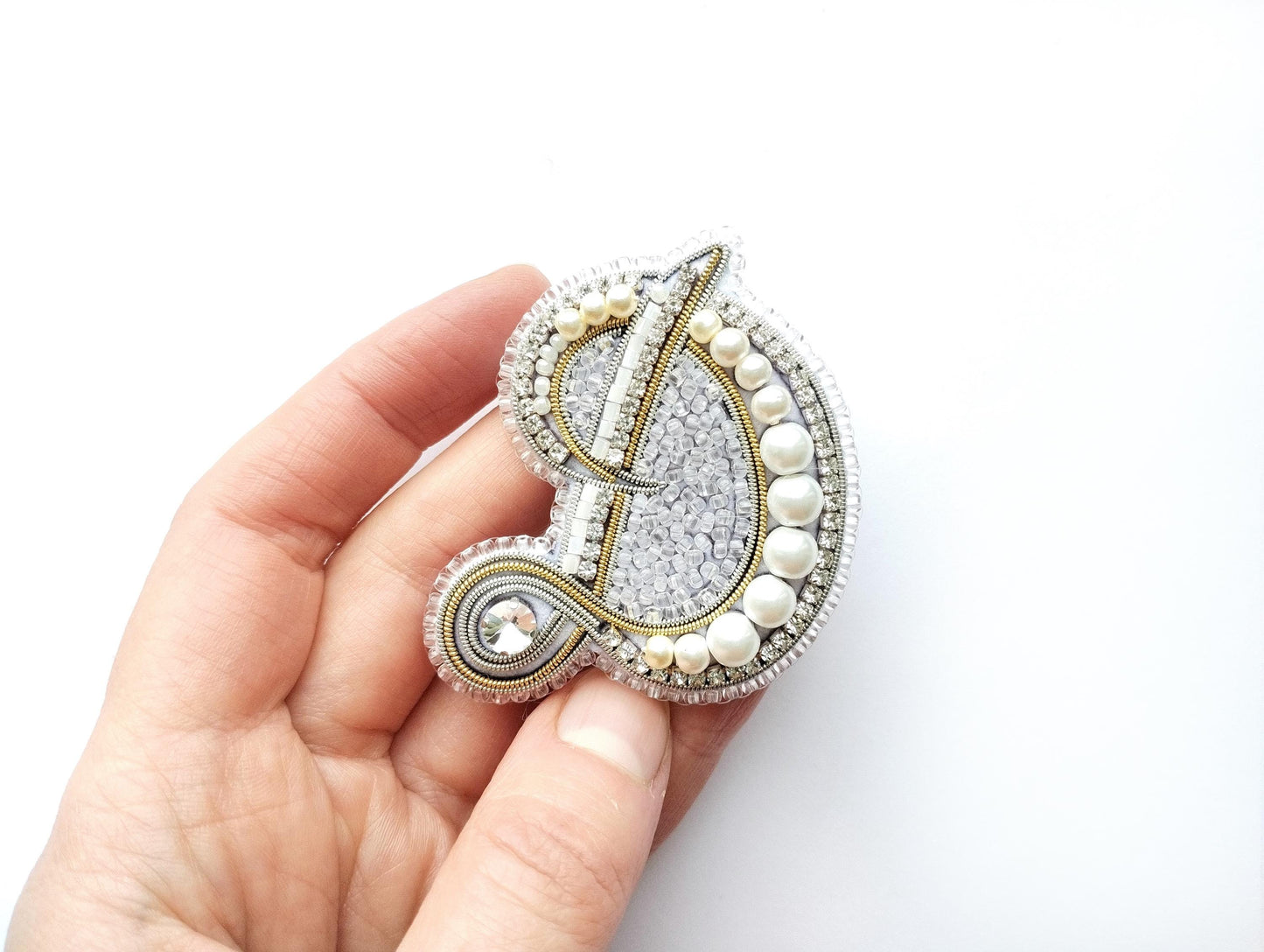 A hand holding a decorative letter D made of beads, pearls, and crystals.