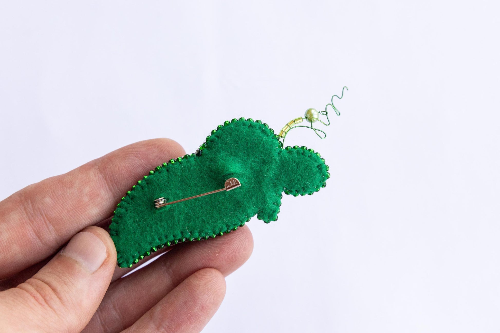 a hand holding a green brooch with a pin