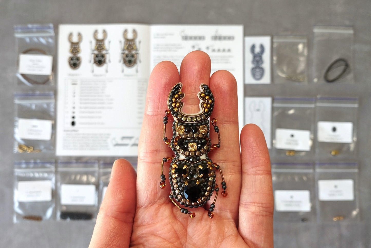 A hand holding a decorative insect brooch with intricate beadwork and a detailed design.