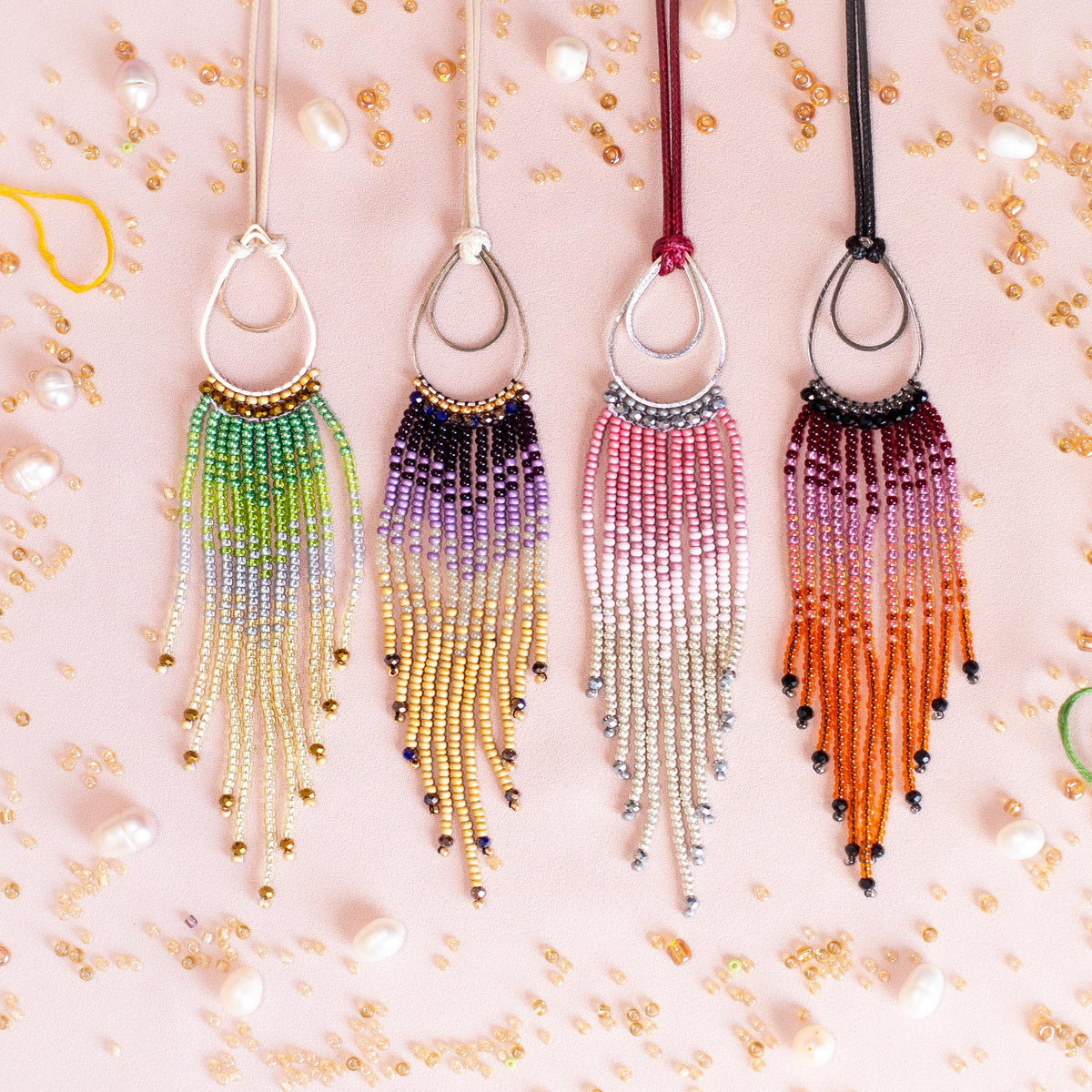 a collection of colorful beaded necklaces with long tassels hanging from them, arranged on a pink background with scattered pearls.