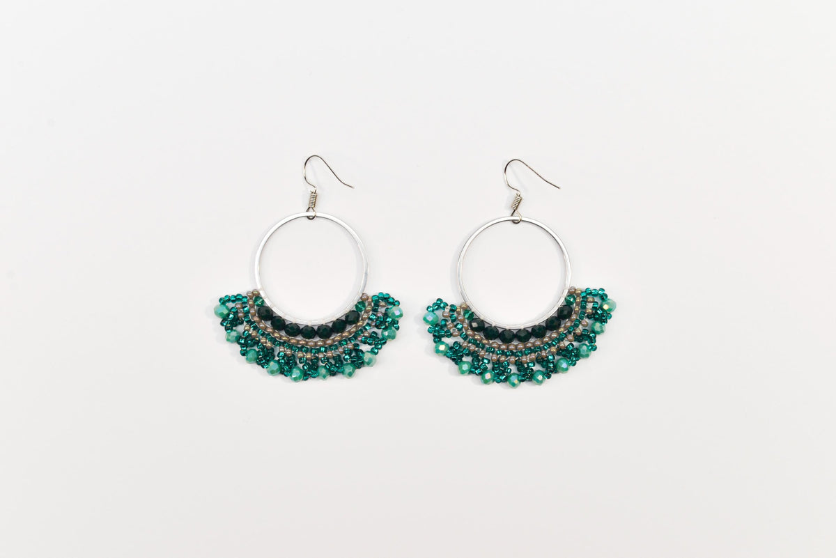 A pair of earrings with a circular hoop design and green beads or stones hanging from the bottom.