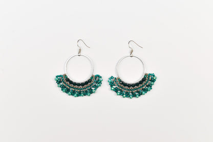 A pair of earrings with a circular hoop design and green beads or stones hanging from the bottom.