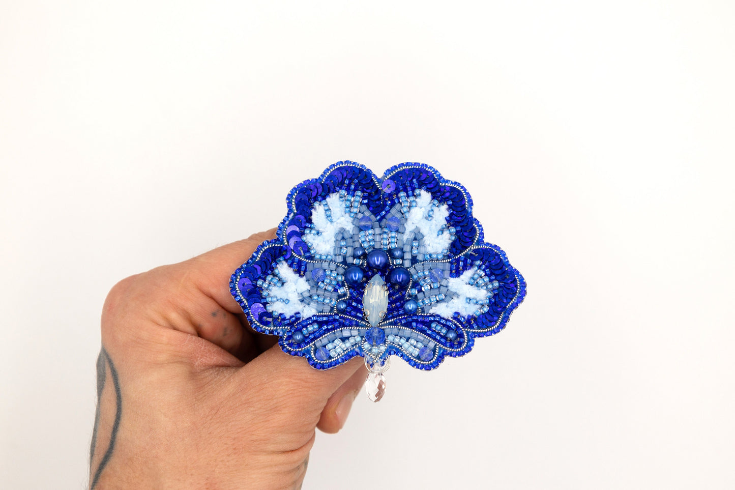 a hand holding a blue and white flower brooch