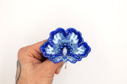 a hand holding a blue and white flower brooch
