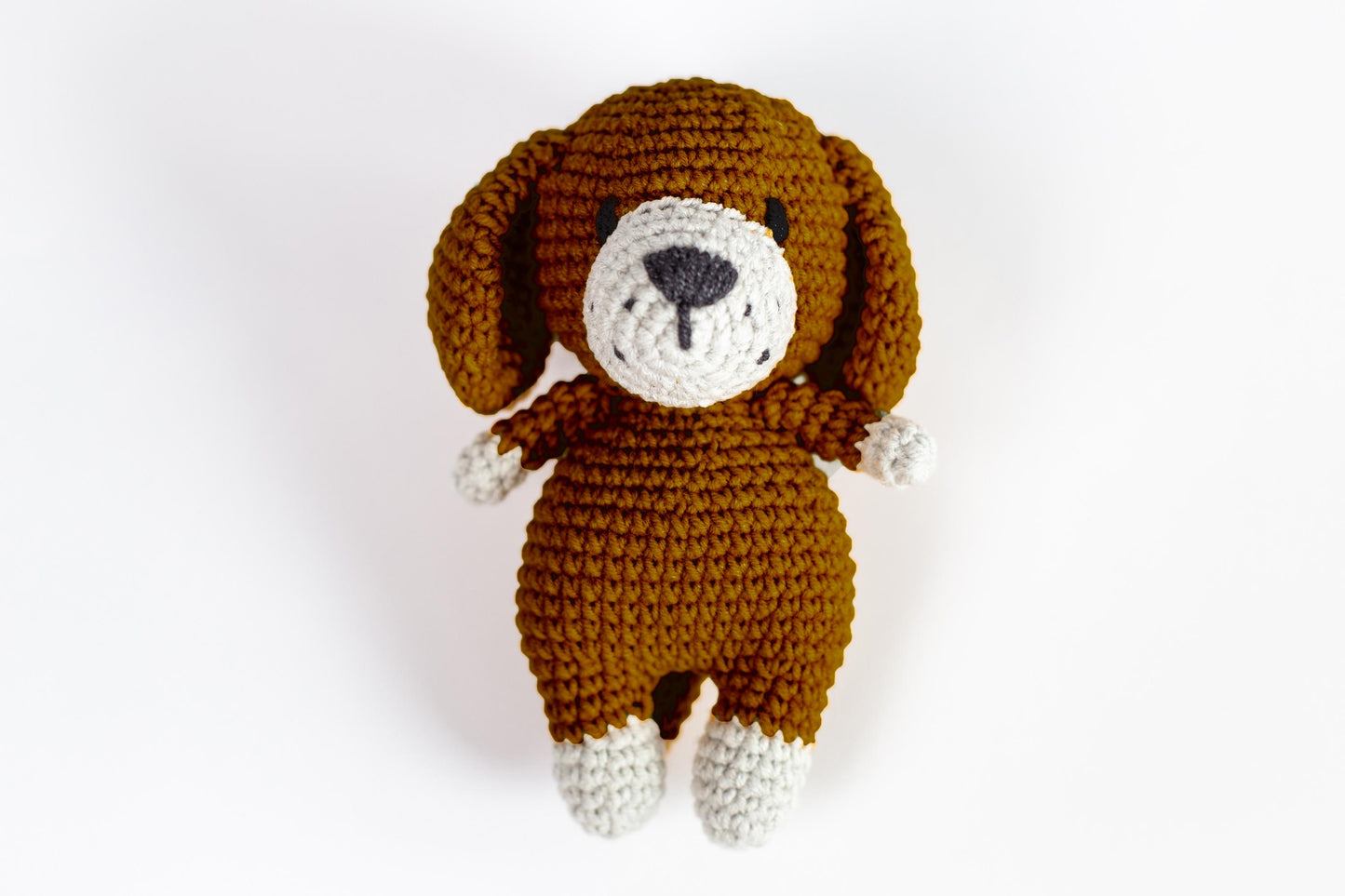 a crocheted brown dog laying down on a white surface