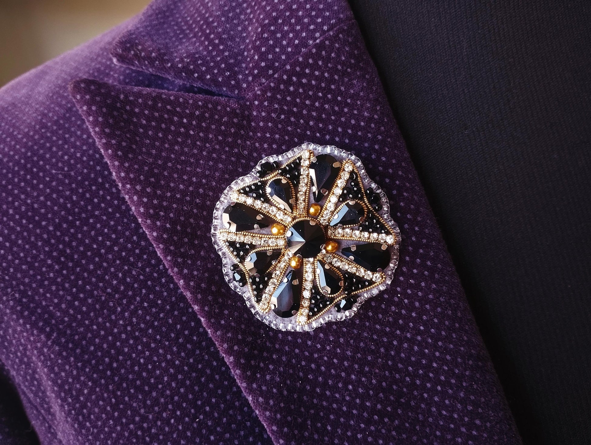 A close-up view of a purple suit jacket with a decorative brooch featuring a black and gold floral design.
