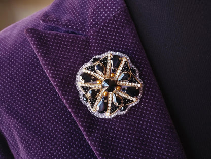 A close-up view of a purple suit jacket with a decorative brooch featuring a black and gold floral design.