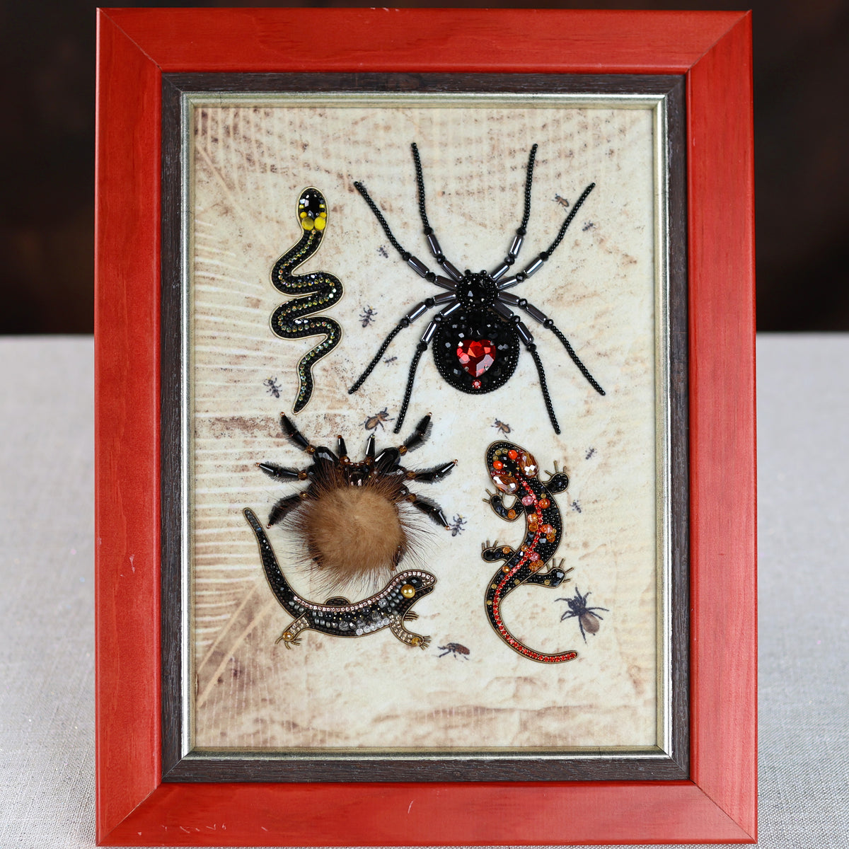 a framed collage of various insects, including a spider, a snake, a lizard, and a tarantula, all displayed together in a red frame.