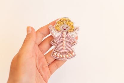 A hand holding a decorative beaded angel figure against a plain white background.