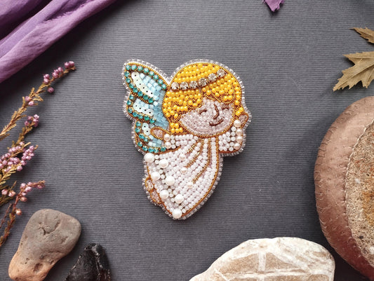 a decorative piece of embroidered art, including a butterfly motif, surrounded by various natural elements such as flowers, rocks, and leaves.