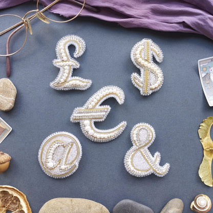 a collection of ornate, beaded, and pearl-embellished objects arranged to spell out the word "LESS THAN 500 CHARACTERS".