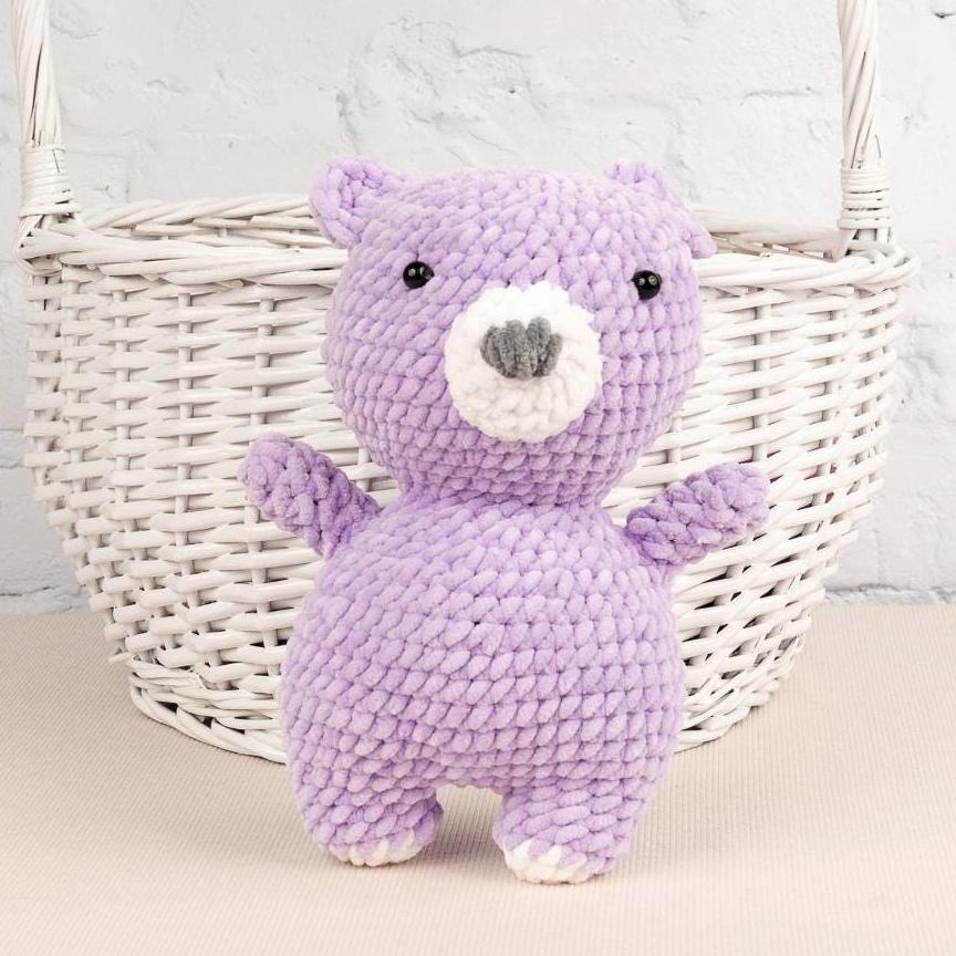 a purple teddy bear sitting next to a ball of yarn