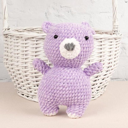 a purple teddy bear sitting next to a ball of yarn