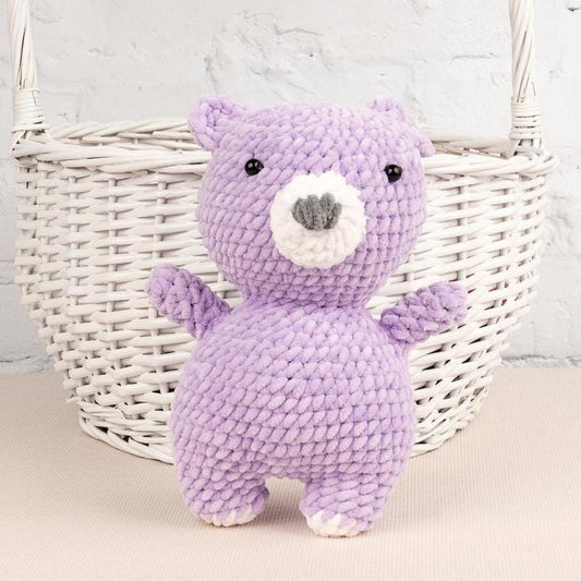 a purple teddy bear sitting next to a ball of yarn