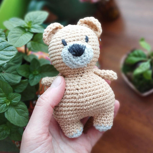 a hand holding a small crocheted teddy bear