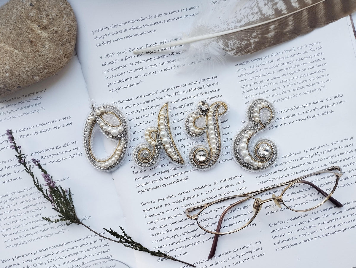 a close-up of a book with text in Russian, a feather, a pair of glasses, and some decorative elements such as pearls and beads.