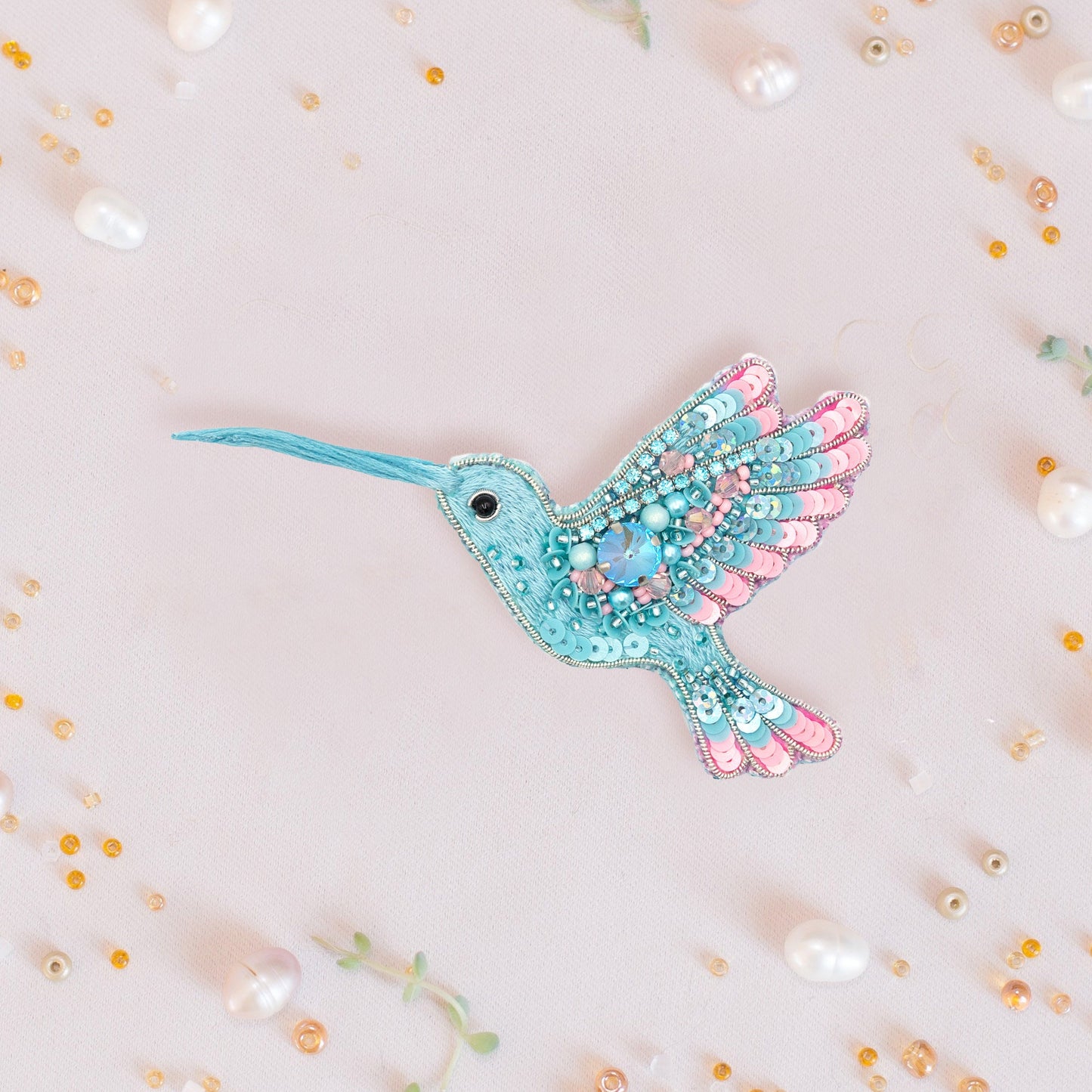 a blue and pink bird brooch sitting on top of a white surface