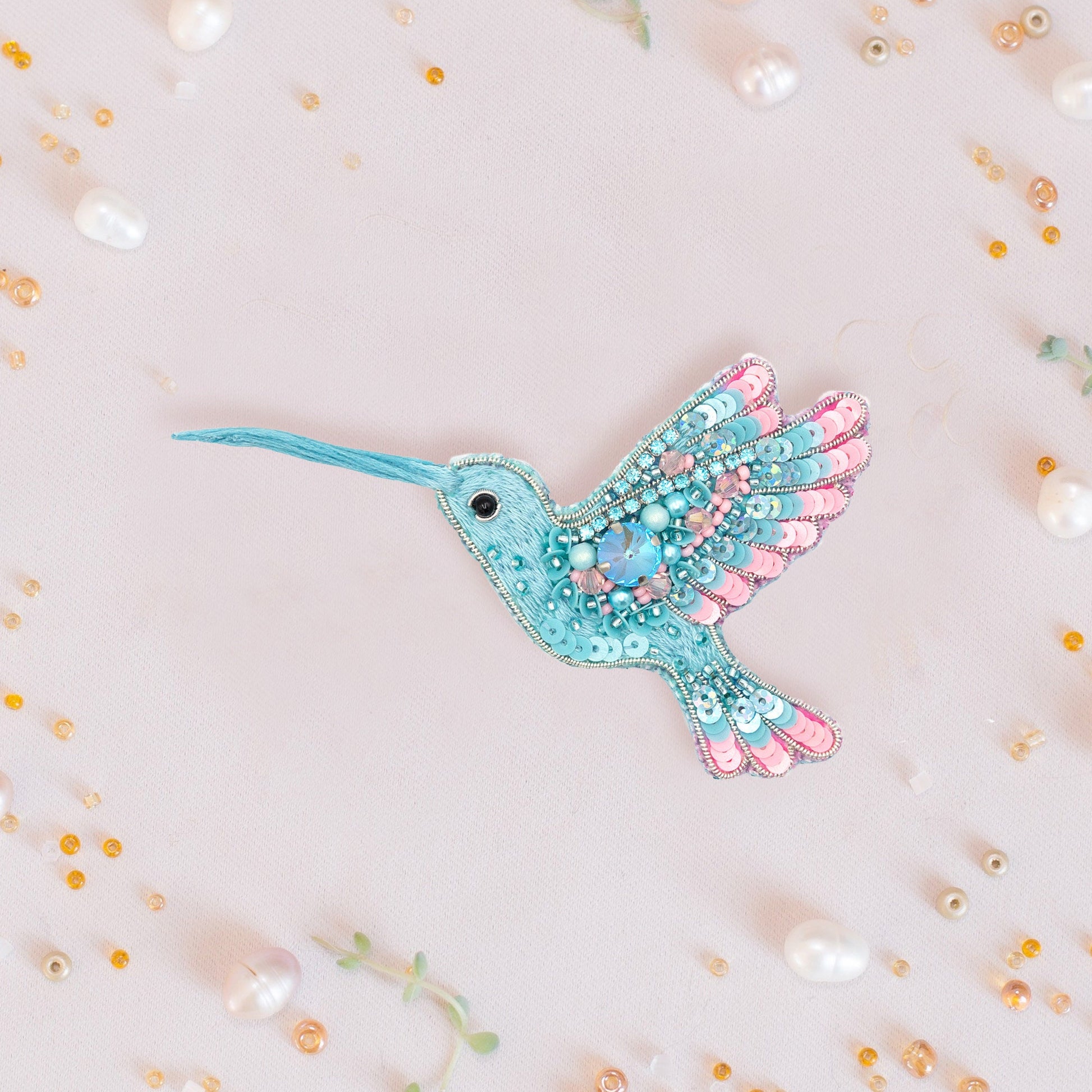 a blue and pink bird brooch sitting on top of a white surface
