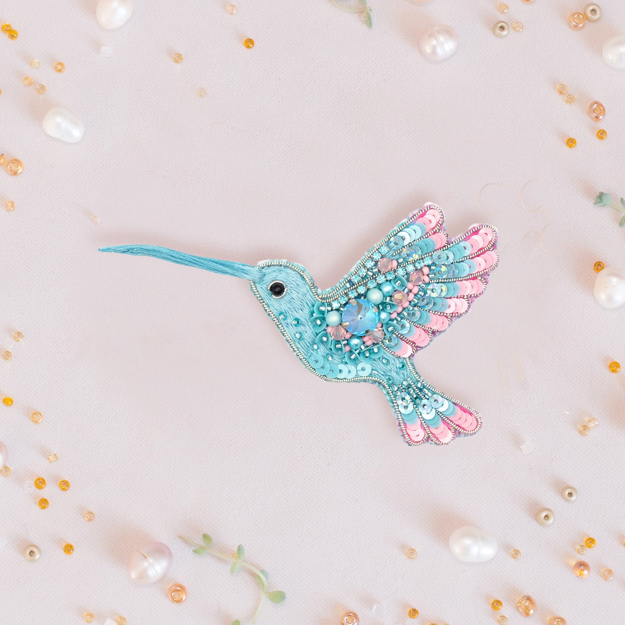 a blue and pink bird brooch sitting on top of a white surface