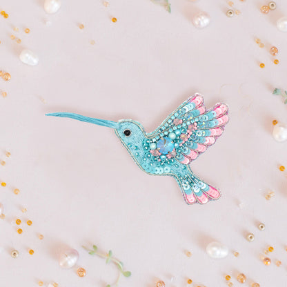a blue and pink bird brooch sitting on top of a white surface