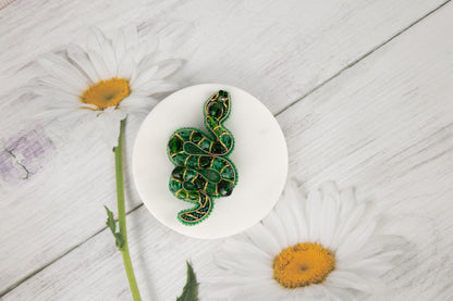 a green snake brooch sitting on top of a white plate