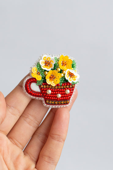 a hand holding a red and white pin with flowers in it