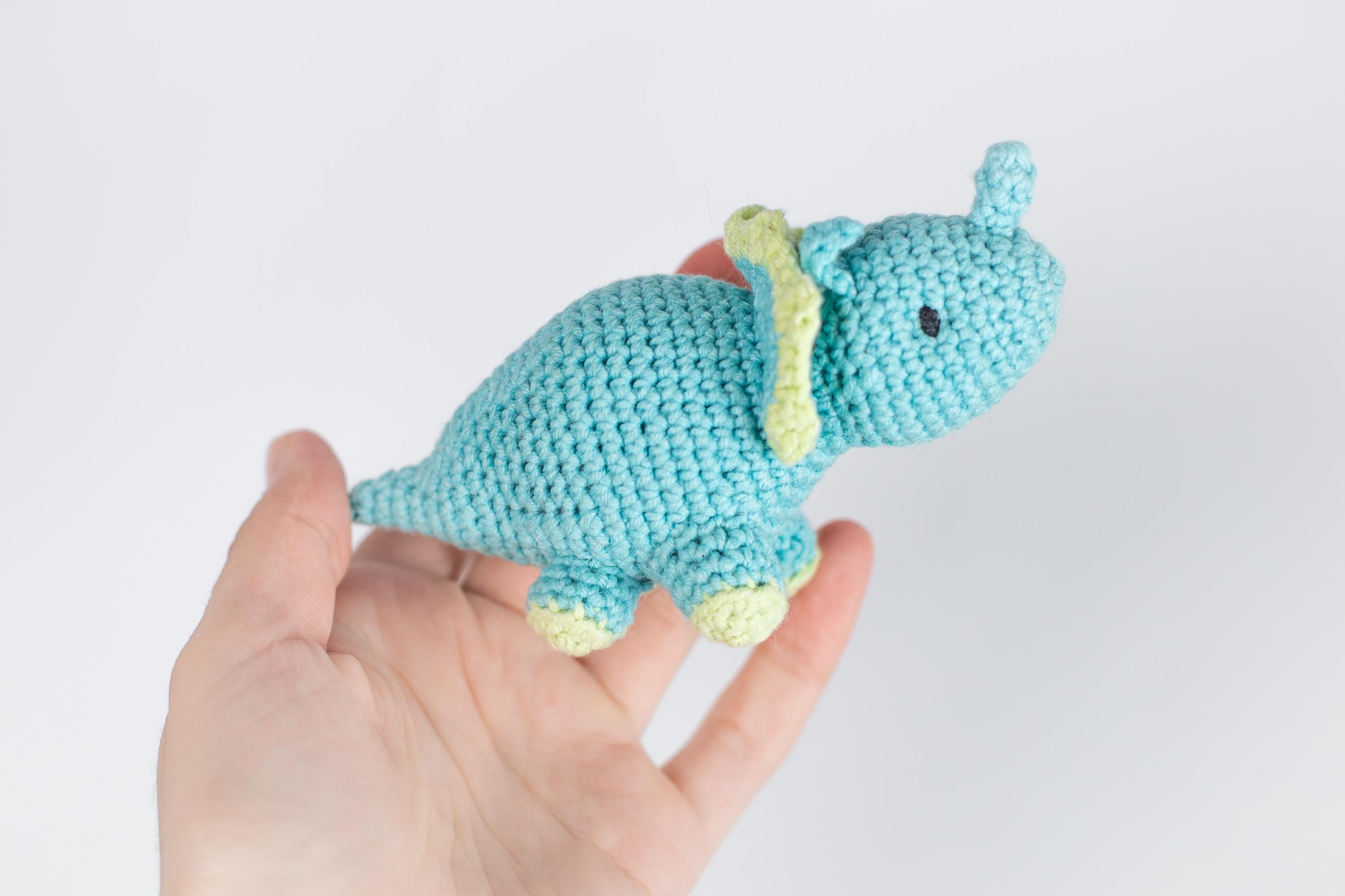 a crocheted blue elephant is held in a hand