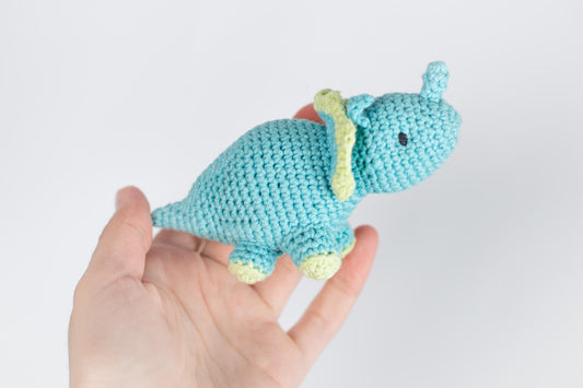 a crocheted blue elephant is held in a hand